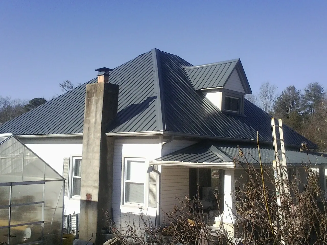 Dark blue standing seam metal roof on a white farmhouse with dormer — Slate & Tile Roof Repair by Roofing Brothers in Eastlake Weir