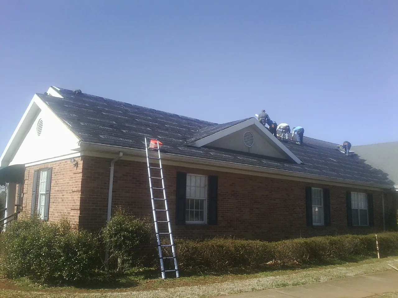 Crew tearing shingles off a brick ranch roof with a ladder set — Emergency Roof Repair work by our crew in Eastlake Weir