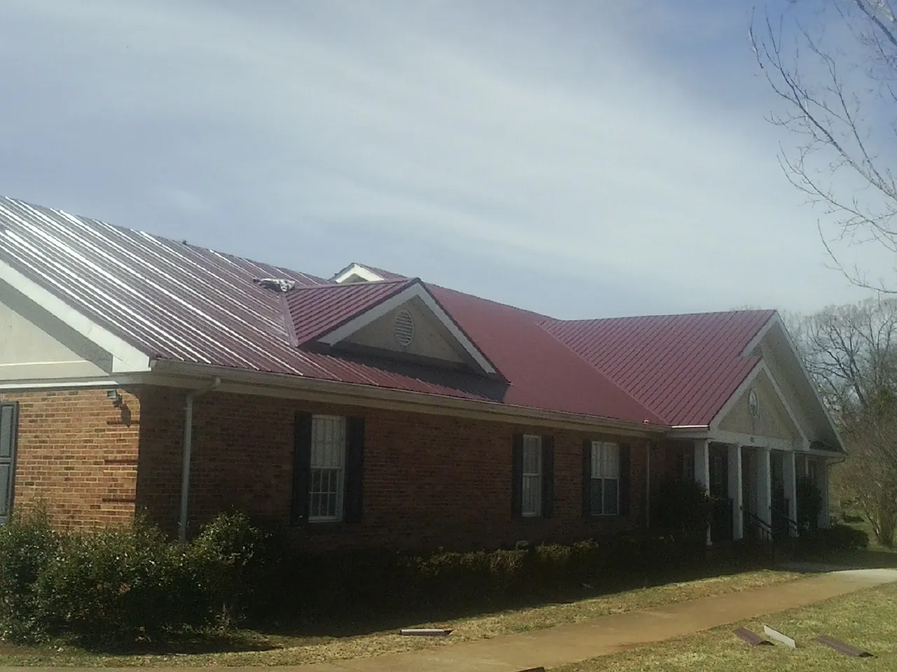 Red metal roof with gabled entries on a long brick building, from a Hail Damage Roof Repair job in Eastlake Weir