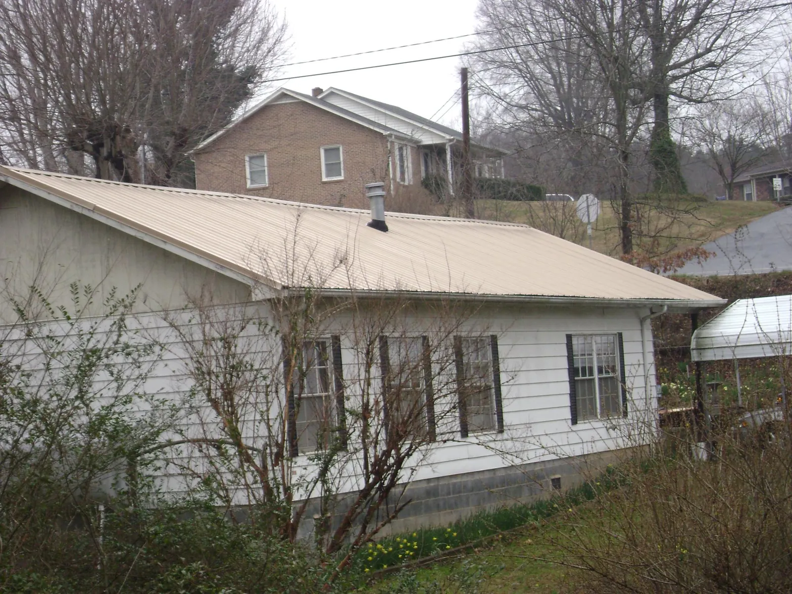 Tan metal roof on a white sided house set into a hillside — Commercial Roofing by Roofing Brothers in Eastlake Weir